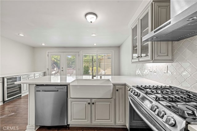 kitchen with sink, tasteful backsplash, beverage cooler, wall chimney range hood, and appliances with stainless steel finishes