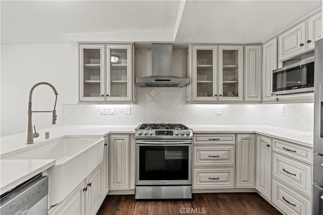 kitchen featuring sink, backsplash, wall chimney range hood, appliances with stainless steel finishes, and dark hardwood / wood-style floors