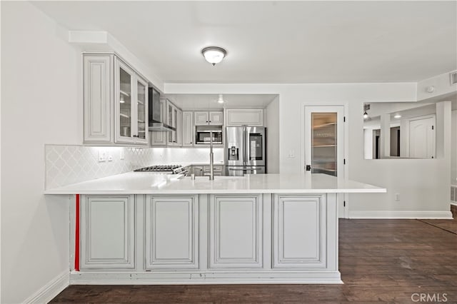 kitchen with appliances with stainless steel finishes, kitchen peninsula, dark wood-type flooring, and wall chimney range hood