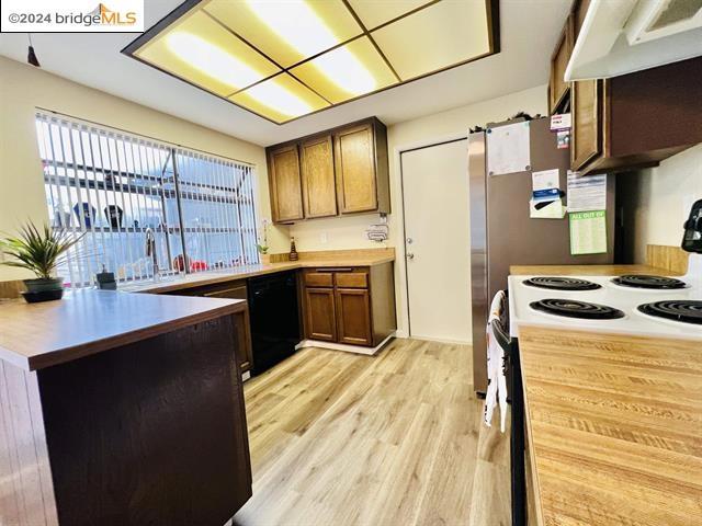 kitchen with black dishwasher, light hardwood / wood-style floors, a barn door, exhaust hood, and white range with electric stovetop