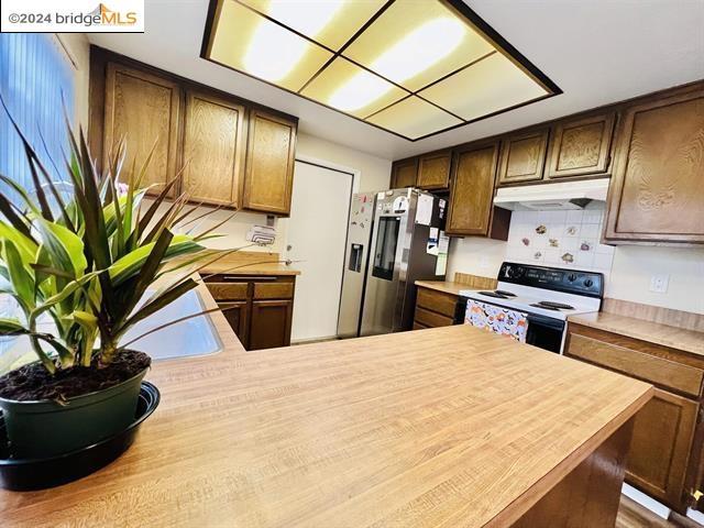 kitchen featuring kitchen peninsula, white range with electric cooktop, stainless steel fridge with ice dispenser, and tasteful backsplash