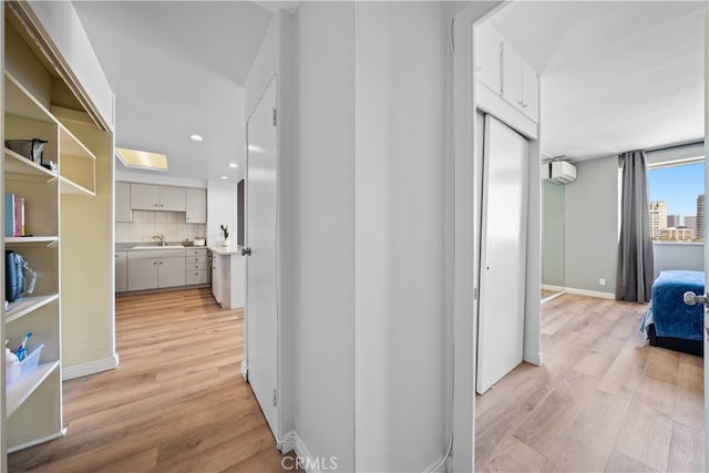 corridor featuring a wall mounted AC, sink, and light wood-type flooring