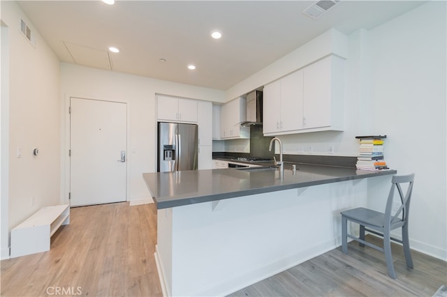 kitchen with white cabinets, wall chimney exhaust hood, kitchen peninsula, and stainless steel fridge with ice dispenser