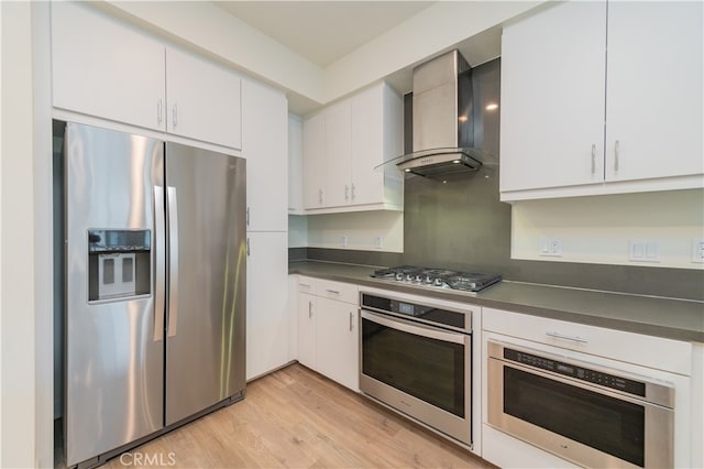 kitchen featuring appliances with stainless steel finishes, wall chimney exhaust hood, light hardwood / wood-style floors, and white cabinetry