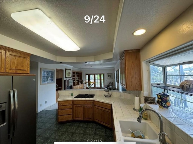 kitchen featuring kitchen peninsula, stainless steel fridge with ice dispenser, tile counters, and a textured ceiling