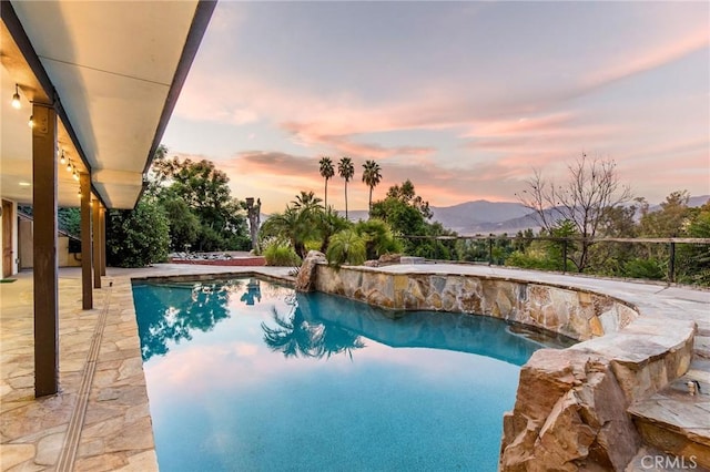 pool at dusk featuring a mountain view and a patio area