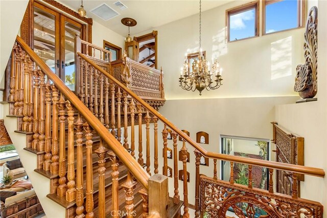 staircase with a high ceiling, a notable chandelier, and a healthy amount of sunlight