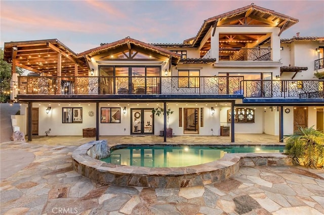 back house at dusk with a balcony and a patio