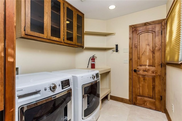 laundry area featuring washing machine and dryer, light tile patterned floors, and cabinets