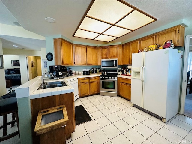 kitchen with kitchen peninsula, stainless steel appliances, sink, light tile patterned floors, and a breakfast bar area