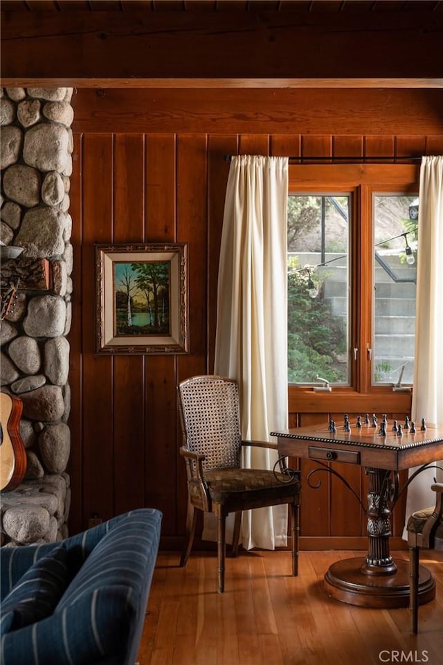 sitting room with wooden walls, beamed ceiling, and hardwood / wood-style flooring