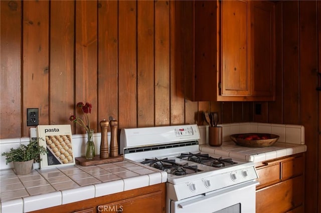 kitchen featuring white range with gas cooktop, wooden walls, and tile countertops