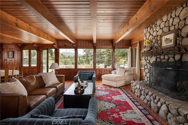 living room featuring beam ceiling, a stone fireplace, hardwood / wood-style floors, wooden walls, and wood ceiling