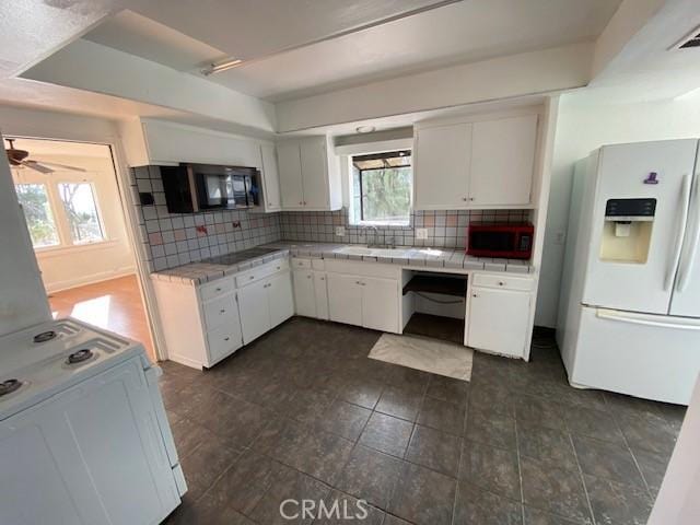 kitchen with backsplash, white cabinets, black appliances, and tile counters