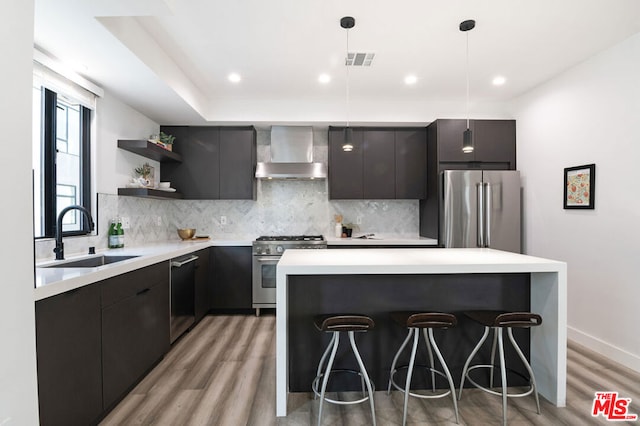 kitchen with sink, wall chimney exhaust hood, stainless steel appliances, light hardwood / wood-style flooring, and pendant lighting