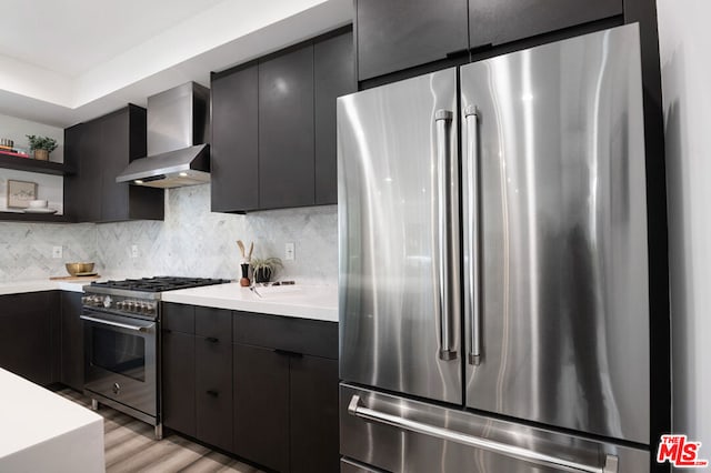 kitchen featuring tasteful backsplash, light hardwood / wood-style flooring, wall chimney exhaust hood, and appliances with stainless steel finishes