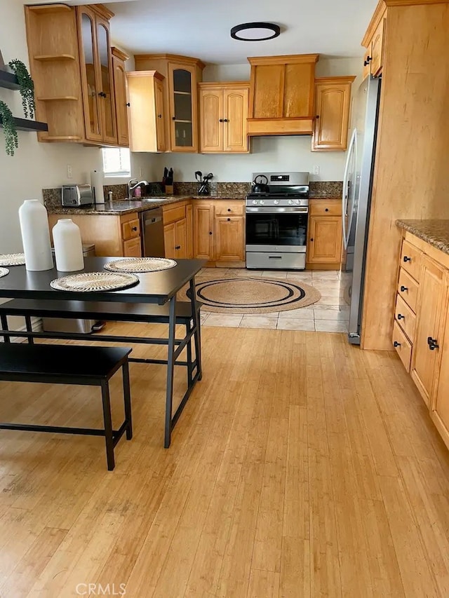 kitchen featuring dark stone counters, light hardwood / wood-style floors, appliances with stainless steel finishes, and sink