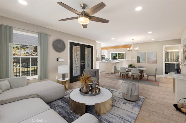 living room with french doors, ceiling fan with notable chandelier, and light wood-type flooring