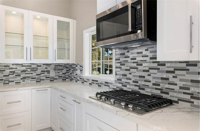 kitchen with stainless steel appliances, light stone counters, glass insert cabinets, and white cabinets