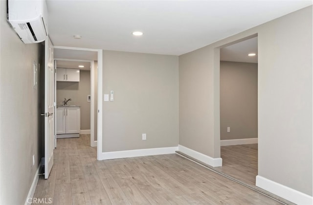 spare room featuring light wood finished floors, baseboards, and an AC wall unit