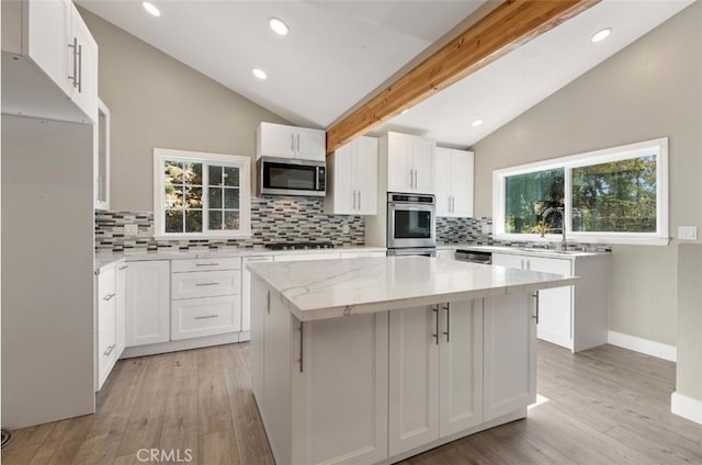 kitchen with lofted ceiling with beams, appliances with stainless steel finishes, white cabinetry, and a center island