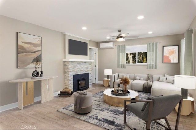 living room with ceiling fan, a wall mounted AC, light hardwood / wood-style flooring, and a wood stove