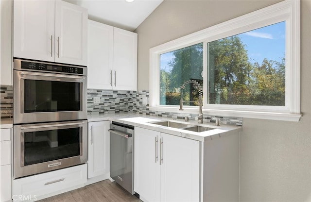 kitchen featuring light wood finished floors, a sink, stainless steel appliances, white cabinetry, and backsplash