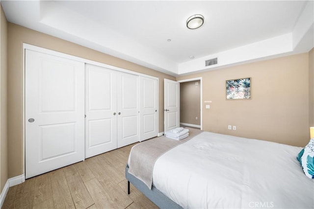 bedroom featuring a closet, a tray ceiling, and light hardwood / wood-style flooring