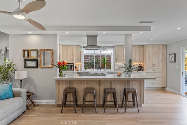 kitchen with a wealth of natural light, light brown cabinets, island range hood, and light hardwood / wood-style flooring