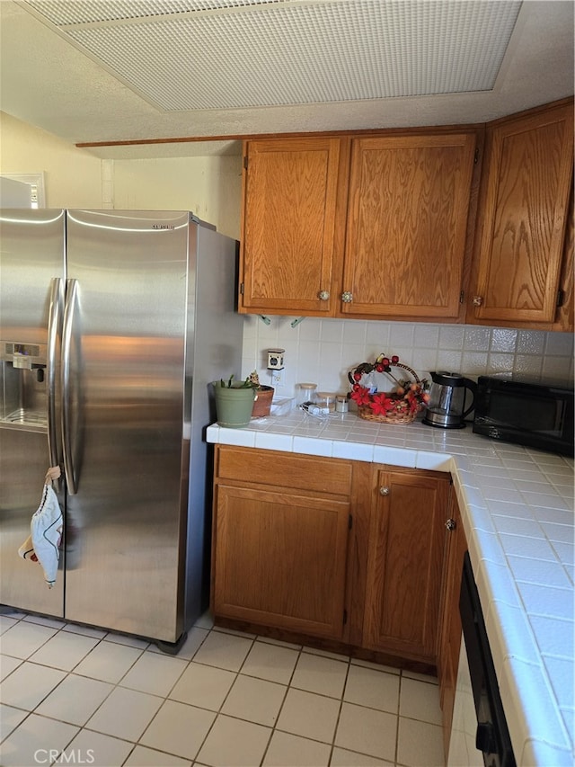 kitchen with tasteful backsplash, light tile patterned floors, exhaust hood, tile counters, and stainless steel fridge with ice dispenser