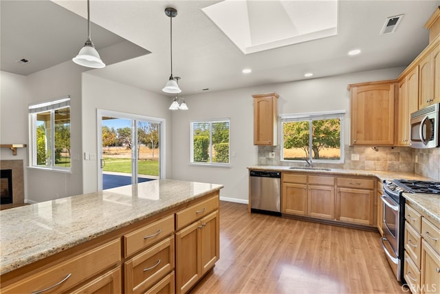 kitchen featuring appliances with stainless steel finishes, hanging light fixtures, light hardwood / wood-style floors, decorative backsplash, and light stone counters