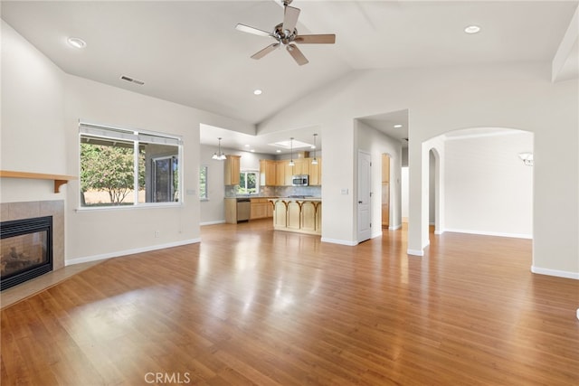 unfurnished living room featuring ceiling fan, light hardwood / wood-style flooring, vaulted ceiling, and a tile fireplace