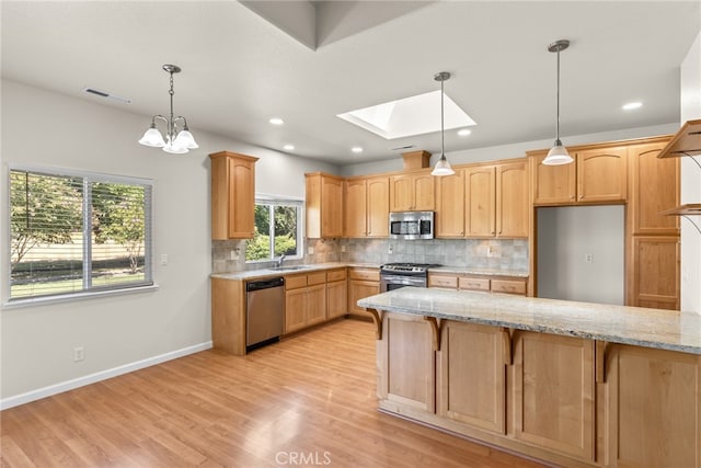 kitchen with light stone counters, a notable chandelier, light hardwood / wood-style flooring, a skylight, and appliances with stainless steel finishes