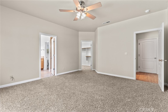 unfurnished bedroom featuring a closet, light colored carpet, ensuite bath, a spacious closet, and ceiling fan