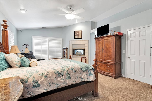 bedroom with ceiling fan, lofted ceiling, a tiled fireplace, and carpet flooring