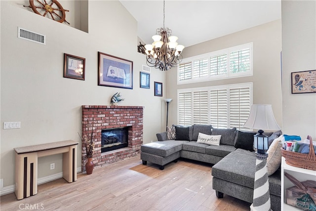 living room with a fireplace, high vaulted ceiling, light wood-type flooring, and a chandelier