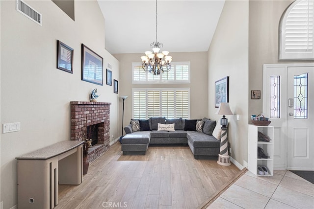 living room with high vaulted ceiling, light hardwood / wood-style flooring, an inviting chandelier, and a brick fireplace