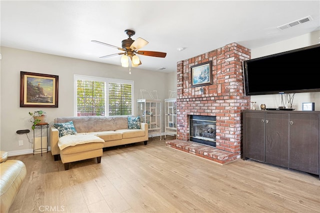 living room featuring ceiling fan, a fireplace, light hardwood / wood-style floors, and brick wall