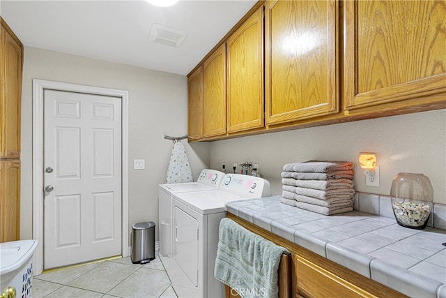 clothes washing area with light tile patterned floors, washing machine and dryer, and cabinets