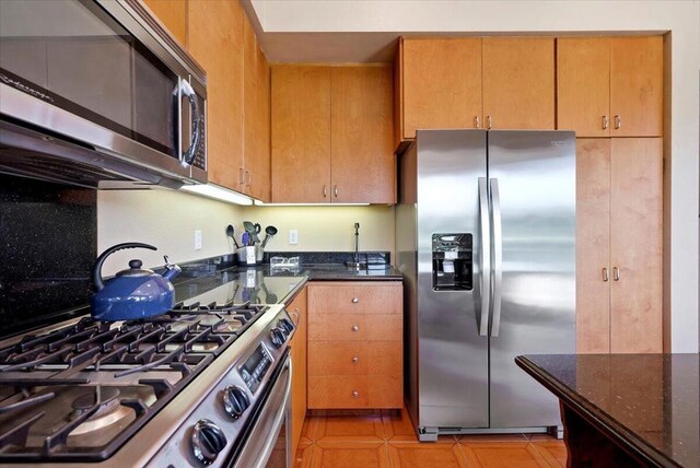 kitchen featuring stainless steel appliances, decorative backsplash, light tile patterned floors, and dark stone counters