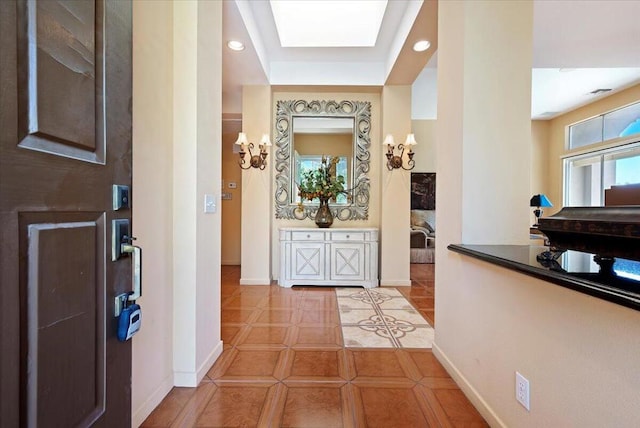 hall with light tile patterned floors, a skylight, plenty of natural light, and a raised ceiling