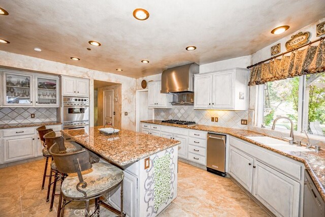 kitchen with light tile patterned floors, a center island, light stone counters, sink, and wall chimney range hood