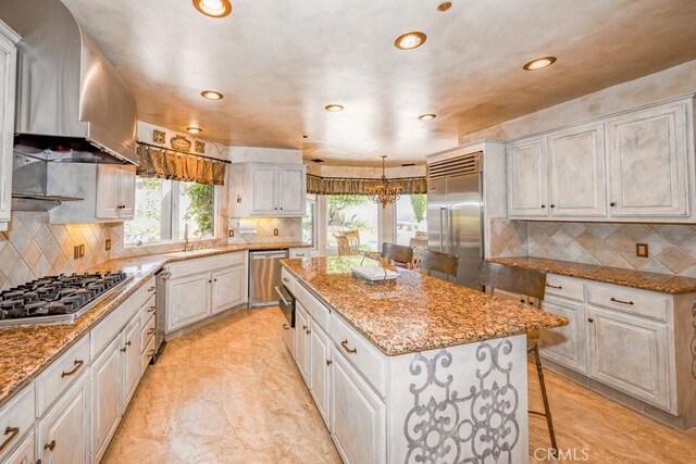 kitchen with a wealth of natural light, a kitchen island, backsplash, and wall chimney range hood