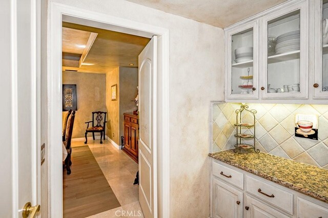 bar featuring tasteful backsplash, light stone counters, light hardwood / wood-style floors, and white cabinetry