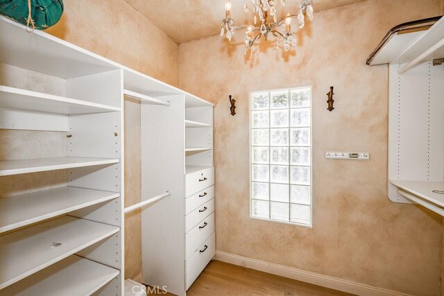 walk in closet with light hardwood / wood-style flooring and a chandelier