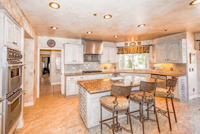 kitchen featuring light stone counters, a center island, appliances with stainless steel finishes, light tile patterned flooring, and wall chimney range hood