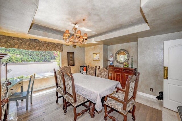 dining space with a raised ceiling, a notable chandelier, and light hardwood / wood-style flooring