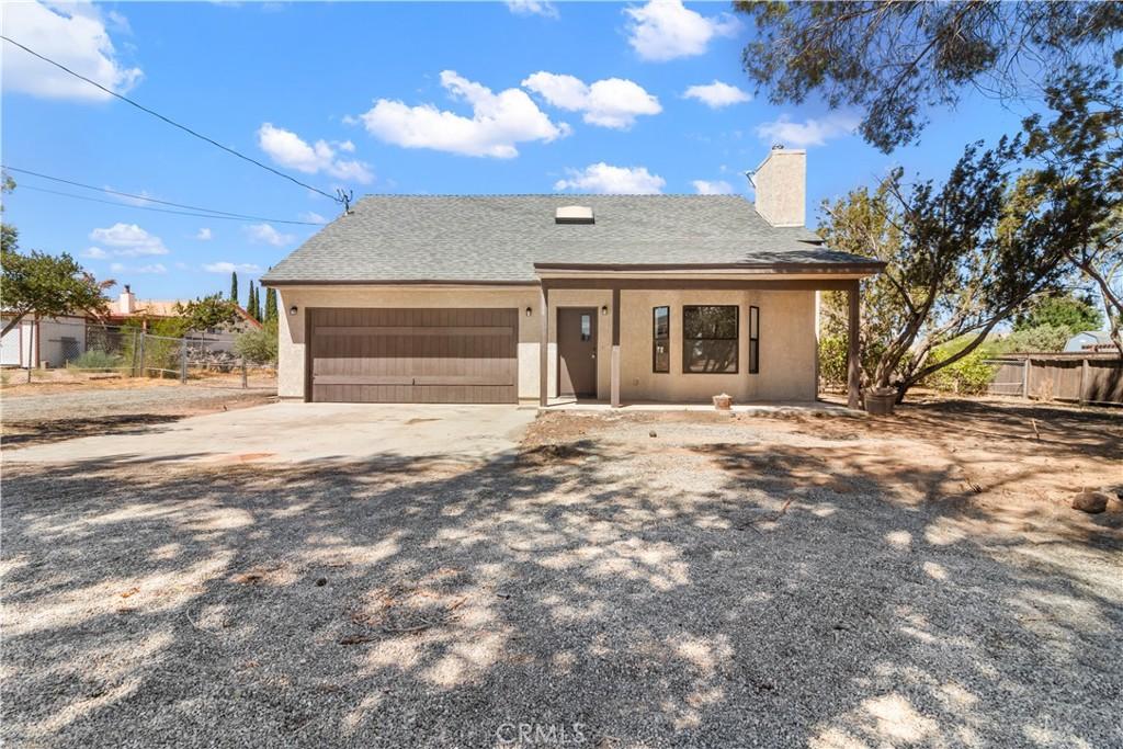 view of front of house featuring driveway, a garage, a chimney, fence, and stucco siding