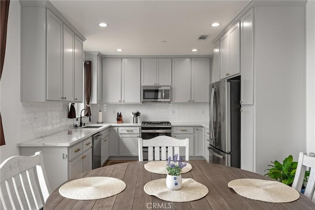 kitchen with sink, tasteful backsplash, light stone counters, gray cabinets, and appliances with stainless steel finishes