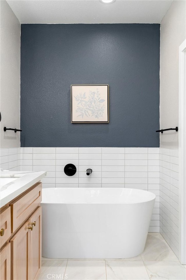 bathroom featuring a tub to relax in, vanity, and tile walls